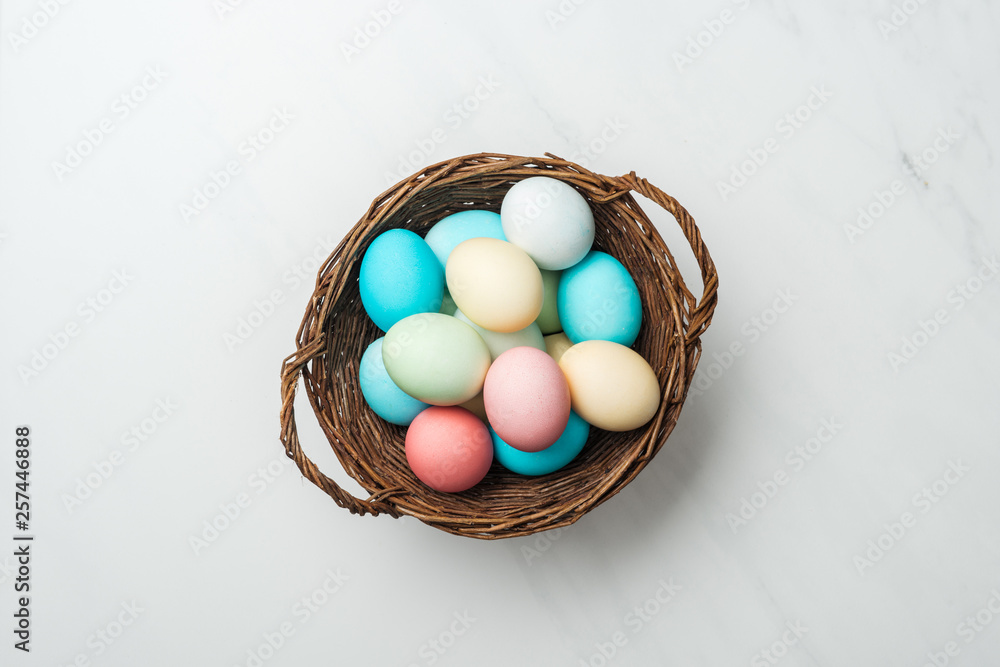 top view of colorful pastel easter eggs in wicker basket on white top view of colorful pastel easter eggs in wicker basket on white