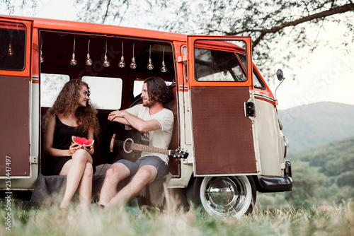 A young couple with guitar outdoors on a roadtrip through countryside, talking. photo