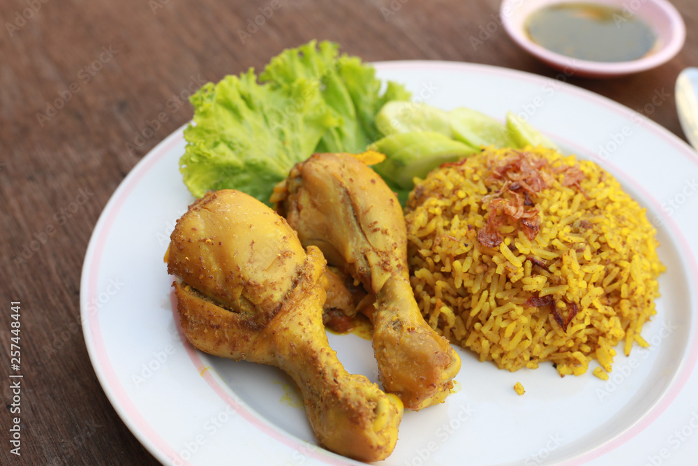 Muslim yellow rice with chicken in a white plate on a wooden floor Muslim yellow rice with chicken in a white plate on a wooden floor