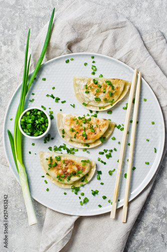 Homemade Korean dumplings, chopsticks, fresh green onions. Gray background, top view