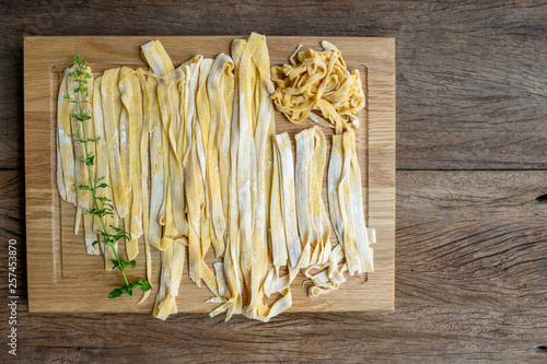 Raw yellow pasta in difference size are placed on wood plate waiting for cooking process.