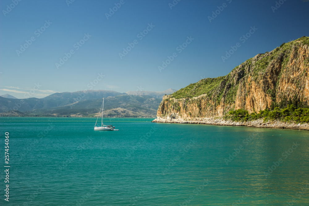 summer cruise vacation Mediterranean sea bay beautiful vivid colors scenery landscape with small walking yacht on calm water surface near waterfront district, mountain background