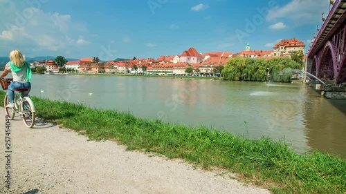 A young woman with blonde hair is having a relaxing day and she is cycling down the path alongside a river. photo