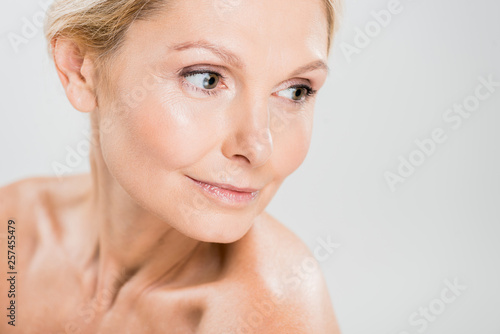 attractive and blonde mature woman looking away isolated on grey