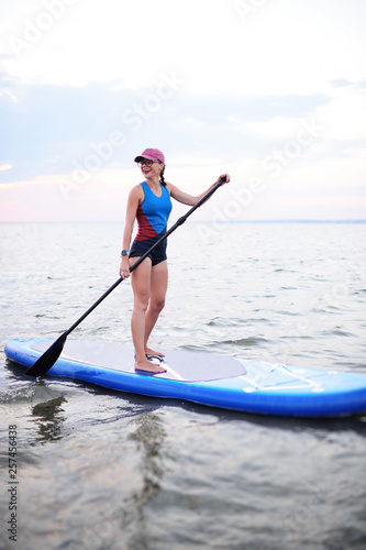 attractive young girl with sup board on the background of the sea and sunset
