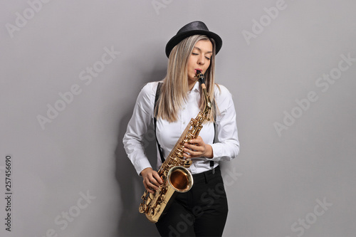 Young female musician playing saxophone and leaning against gray wall