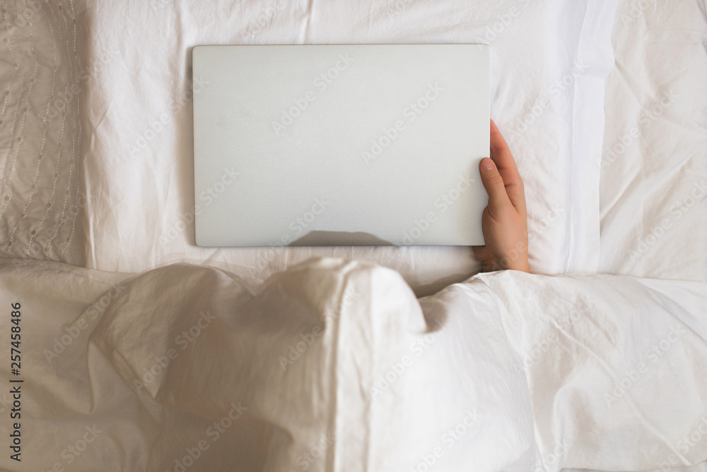 Girl lying with a laptop in bed covered by blanket. Woman can't sleep and have to work late at night. Top view Girl lying with a laptop in bed covered by blanket. Woman can't sleep and have to work late at night. Top view