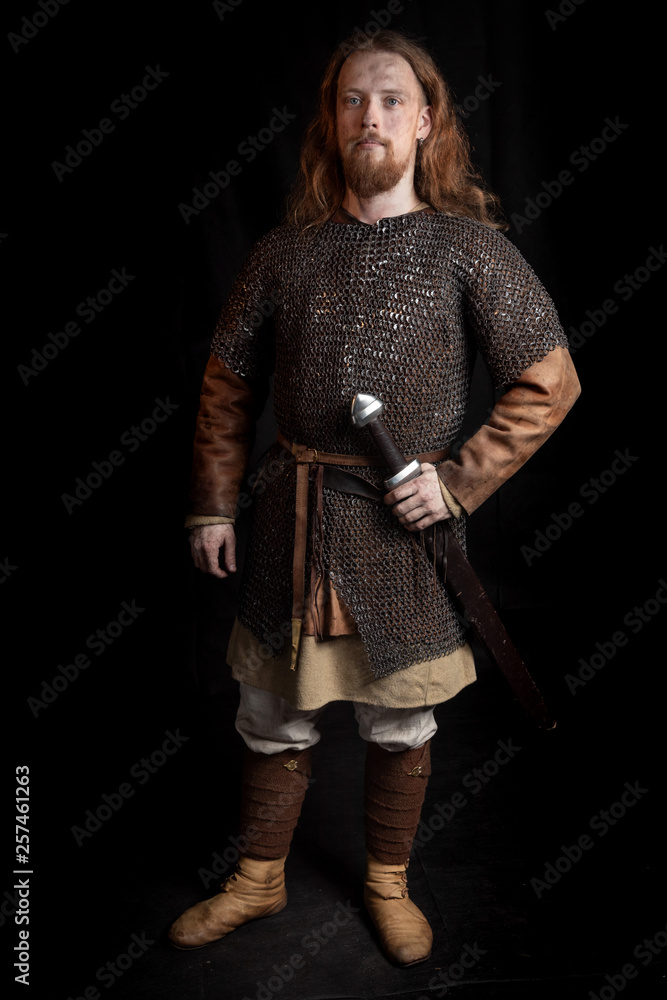 Young long haired redhead viking man in a chain armor, he has a sword on his belt Young long haired redhead viking man in a chain armor, he has a sword on his belt