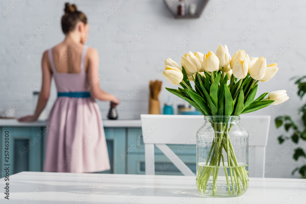 selective focus of bouquet of tulips on kitchen table with woman on background
