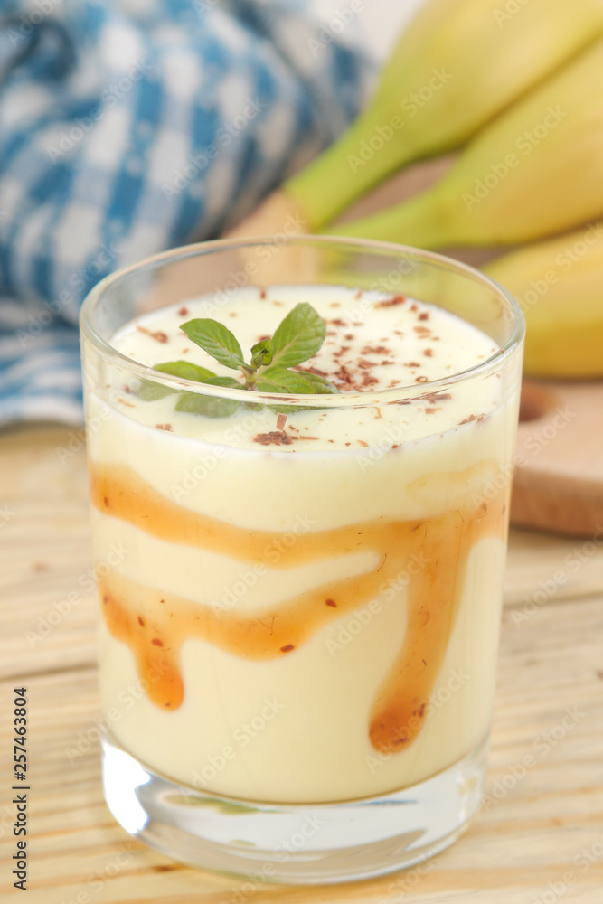 a glass with a banana milkshake, syrup and chocolate chips and a fresh banana on a natural wooden table. Making a milkshake. a glass with a banana milkshake, syrup and chocolate chips and a fresh banana on a natural wooden table. Making a milkshake.