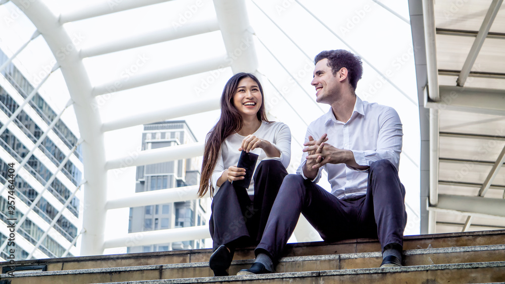 business woman and man sitting on staircase of footbridge.