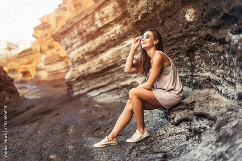 Pretty long hair brunette tourist girl relaxing on the stones near sea.