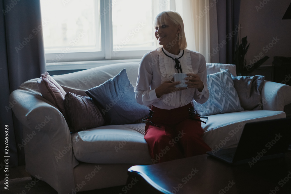 Smiling girl drinking coffee on the couch by the window Smiling girl drinking coffee on the couch by the window