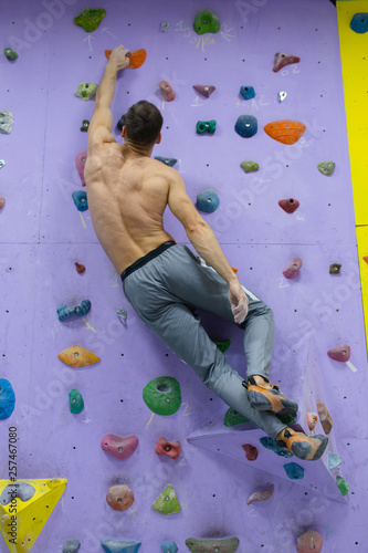 Muscular man practicing rock-climbing on a rock wall indoors