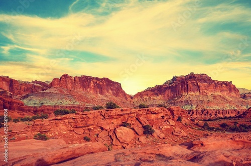 Fototapeta Naklejka Na Ścianę i Meble -  Sunset during golden hour in Southern Utah, sun warming red sandstone, cliffs, mountains, and mesa.  Sun is peaking out behind the rocky peaks