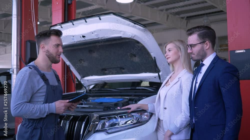 customer service in car workshop, professional technician consult young family client about broken automobile with open hood after repair in service station customer service in car workshop, professional technician consult young family client about broken automobile with open hood after repair in service station