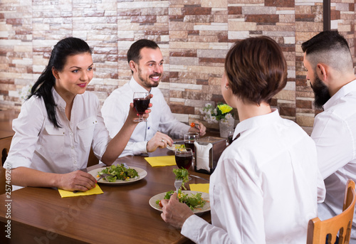 group of joyous friends eating at restaurant and chatting
