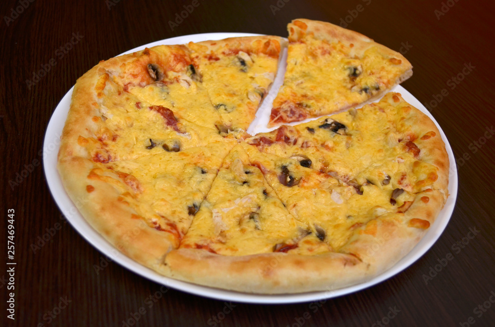 Pizza with cheese and mushrooms on a white plate on a dark wooden table, one piece cut off Pizza with cheese and mushrooms on a white plate on a dark wooden table, one piece cut off