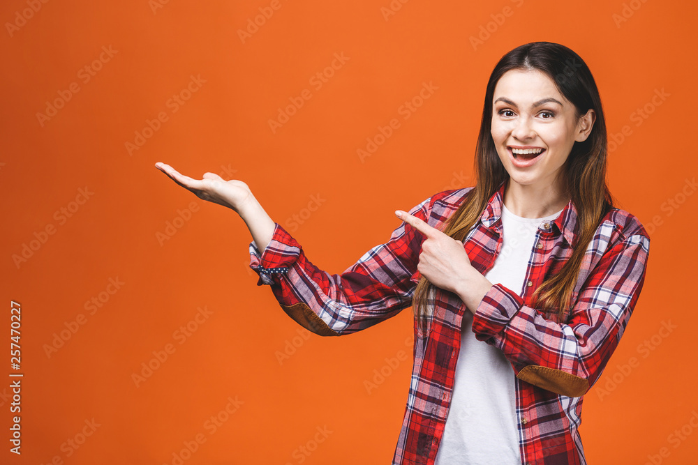 Photo of happy young woman standing isolated over orange wall background. Looking camera showing copyspace pointing. Photo of happy young woman standing isolated over orange wall background. Looking camera showing copyspace pointing.