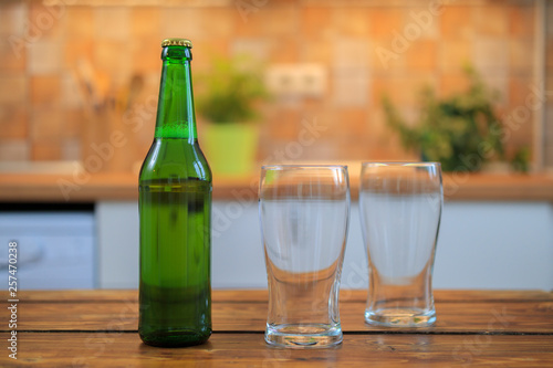 Bottle with beer and empty glasses on the table