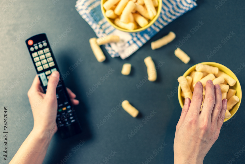 Obraz premium Person with TV remote watching tv and eating chips, romanian pufuleti