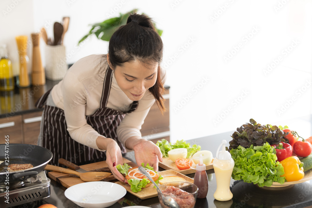 Young woman cooking a hamburger in kitchen with a smile and delicious