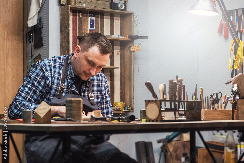 Man working with leather textile at a workshop. Concept of handmade craft production of leather goods. Man working with leather textile at a workshop. Concept of handmade craft production of leather goods.