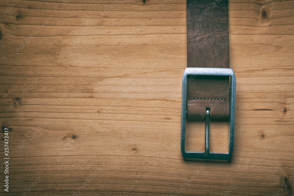 Leather brown belt with a buckle on a wooden board Leather brown belt with a buckle on a wooden board