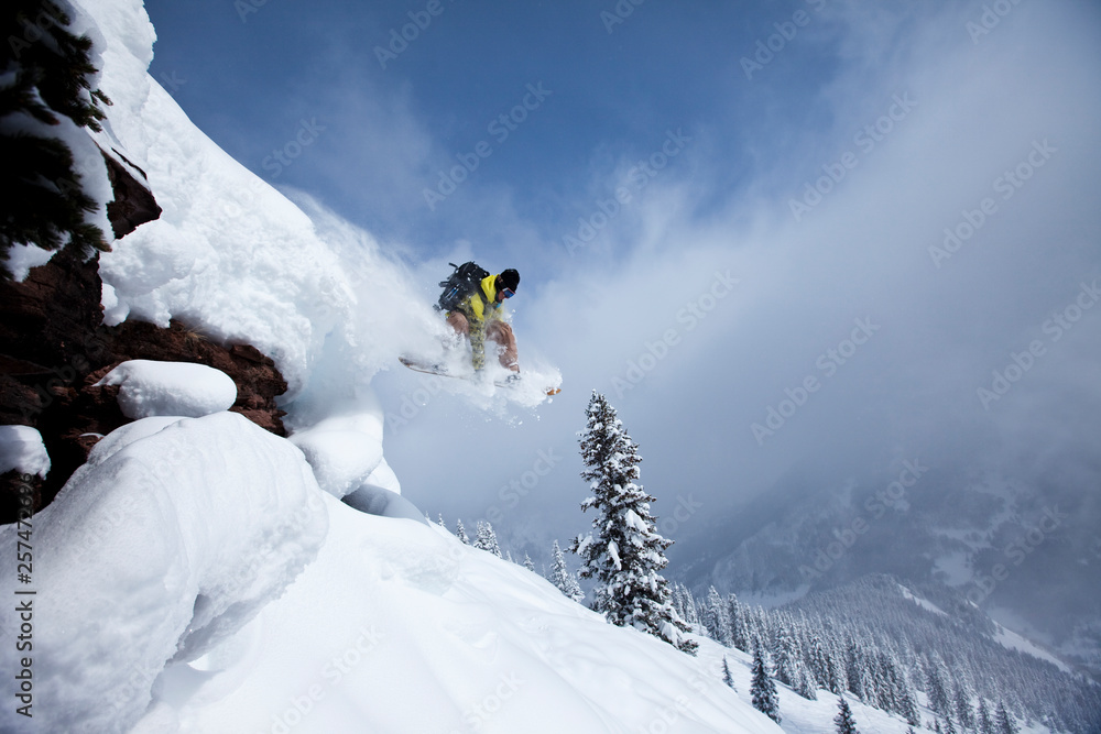 Snowboarder jumps off cliff into powder, Colorado, USA Snowboarder jumps off cliff into powder, Colorado, USA