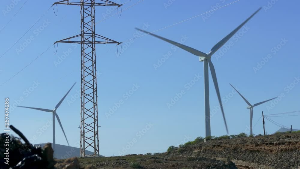 Wind turbines with rotating blades next to electrical towers and power poles on Tenerife, Canary Islands.