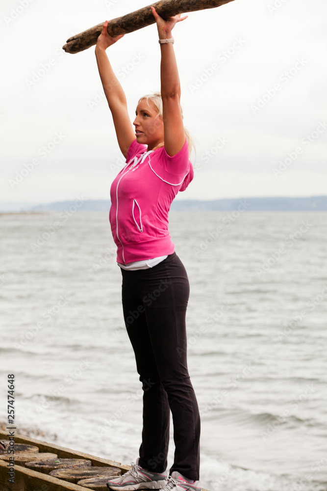 A young, healthy woman uses found driftwood and a narrow bulkhead to exercise on a rustic beach. A young, healthy woman uses found driftwood and a narrow bulkhead to exercise on a rustic beach.