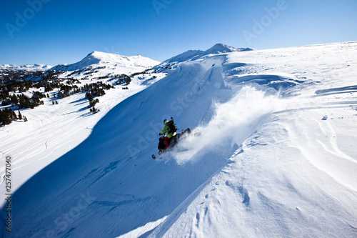 A snowmobiler jumping off a cornice on a sunny winter day in Cooke City, Montana. photo