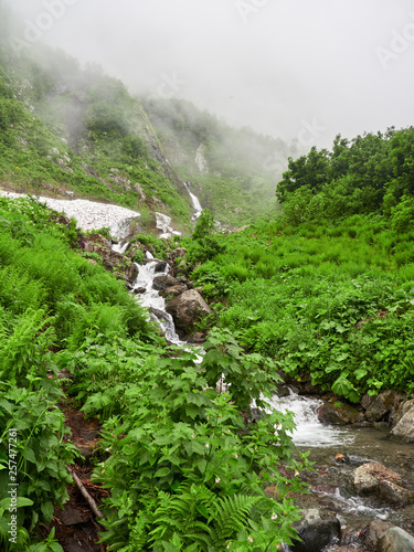 A powerful mountain stream flows down from the rocks in a dense fog.