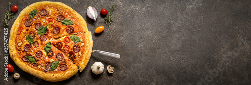 pizza with salami sausage, spinach and cherry tomatoes and tomato sauce on a dark background