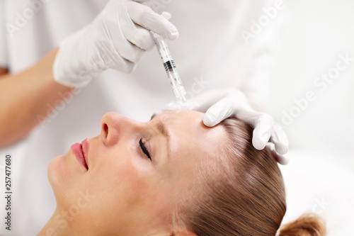 Close up of hands of cosmetologist making botox injection in female forehead