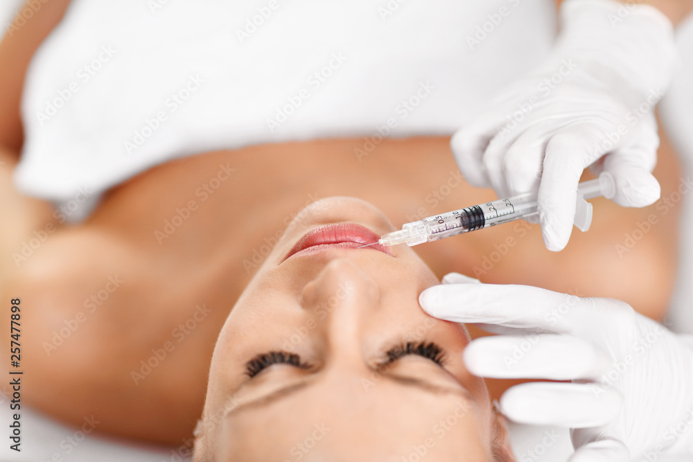 Close up of hands of cosmetologist making botox injection in female lips