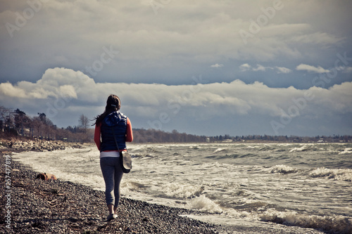 A young woman walks along the shoreline at White Rock Beach, British Columbia, Canada.