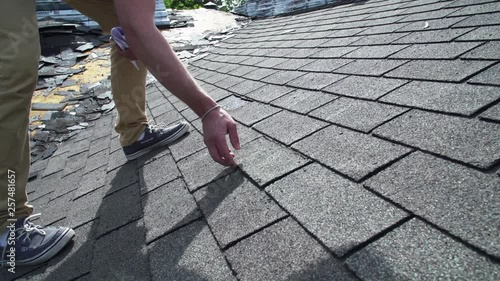 Roof inspector showing damaged shingles on old asphalt roof 