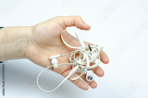 tangled white no brand earphones in a hand on white