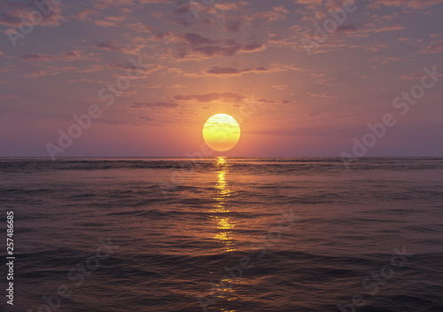 sundown over calm sea with small clouds and godrays