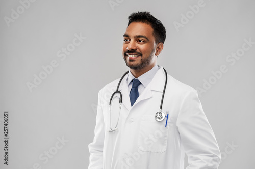 medicine, profession and healthcare concept - smiling indian male doctor in white coat with stethoscope over grey background