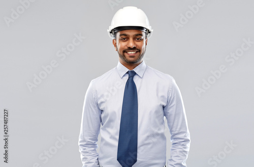 architecture, construction business and building - smiling indian architect or businessman in helmet over grey background © Syda Productions