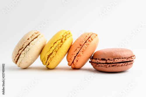 Side view of four sweet French macarons isolated on white, flavours of coconut, vanilla, lemon, orange, caramel and chocolate