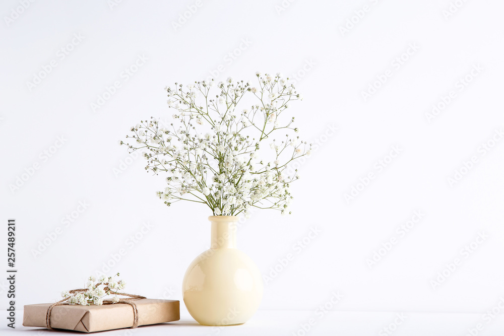 White gypsophila flowers in vase with gift box on grey background White gypsophila flowers in vase with gift box on grey background