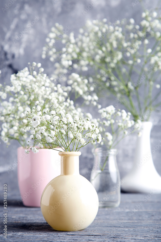 White gypsophila flowers in vases, cup and glass bottle on grey background White gypsophila flowers in vases, cup and glass bottle on grey background
