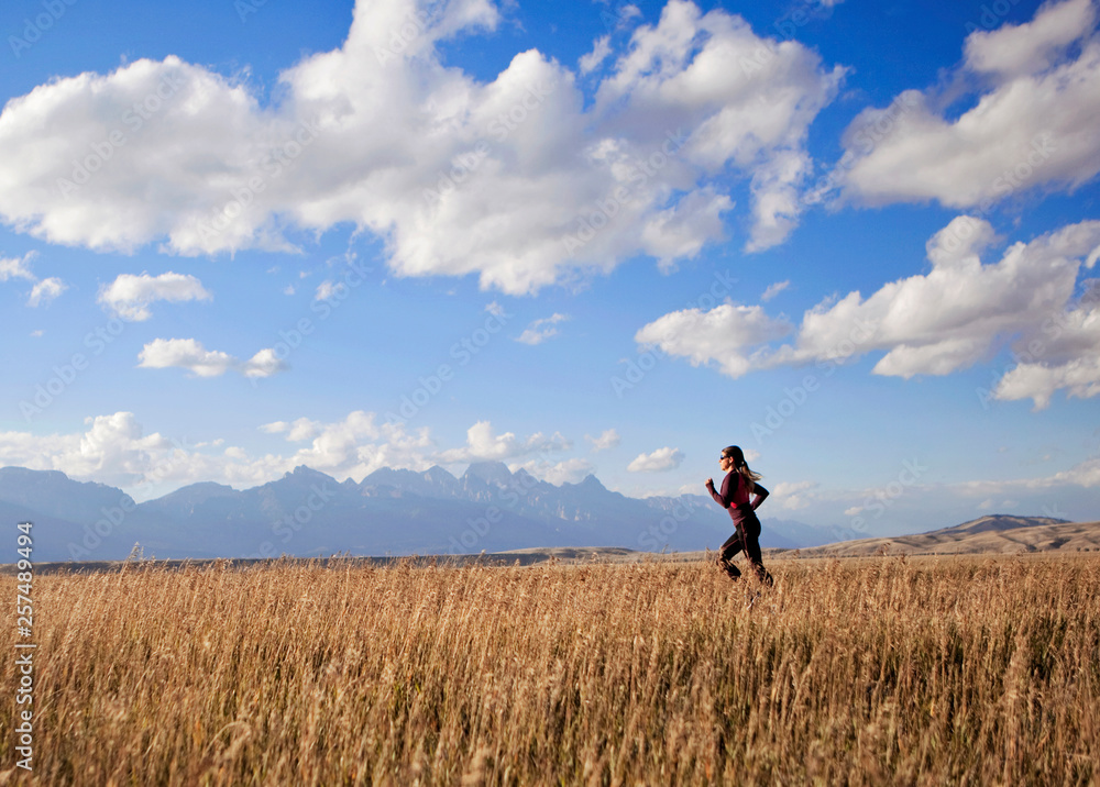 A young woman runs along a dirt road witht the Tetons in the background A young woman runs along a dirt road witht the Tetons in the background