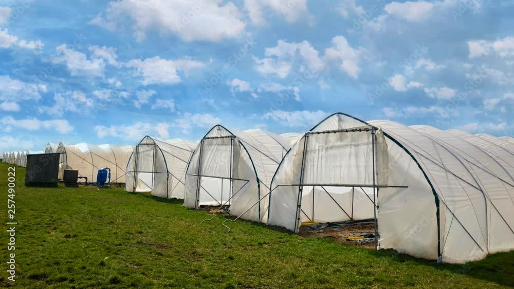 White modern plastic green houses against blue cloudy sky background in early spring. White modern plastic green houses against blue cloudy sky background in early spring.