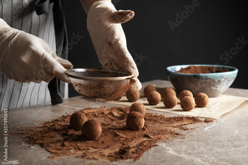 Woman preparing tasty chocolate truffles at table, closeup