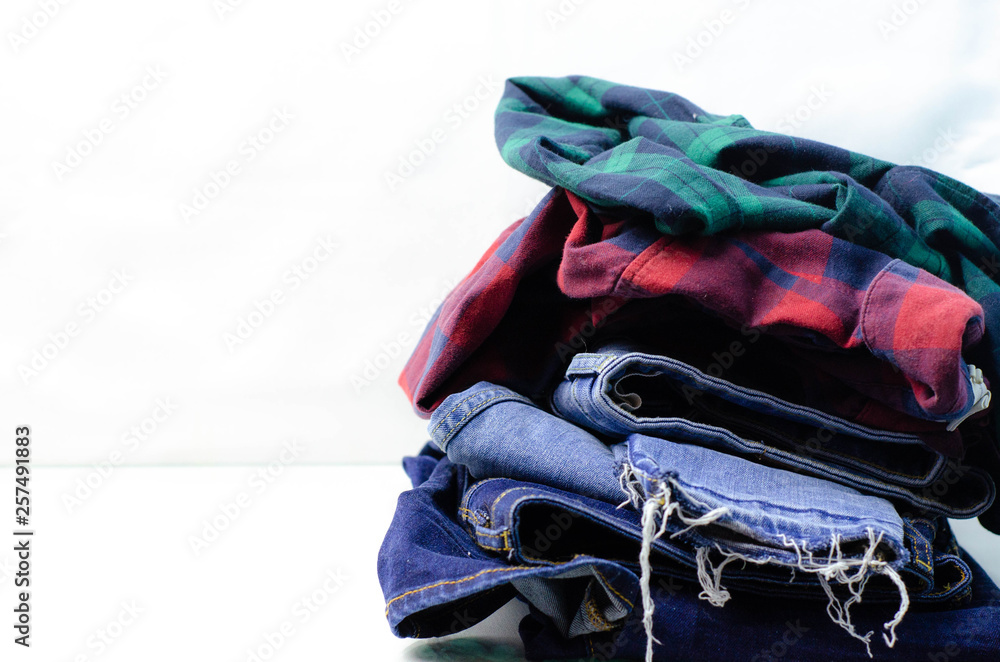 Stack of blue jeans and plaid shirts on white background