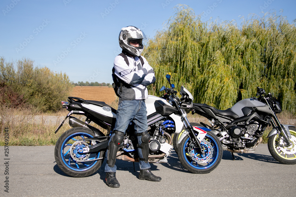 Obraz premium The motorcyclist in helmet on a motorcycle. Journey to a motorcycle. Motorcyclist stands on the road